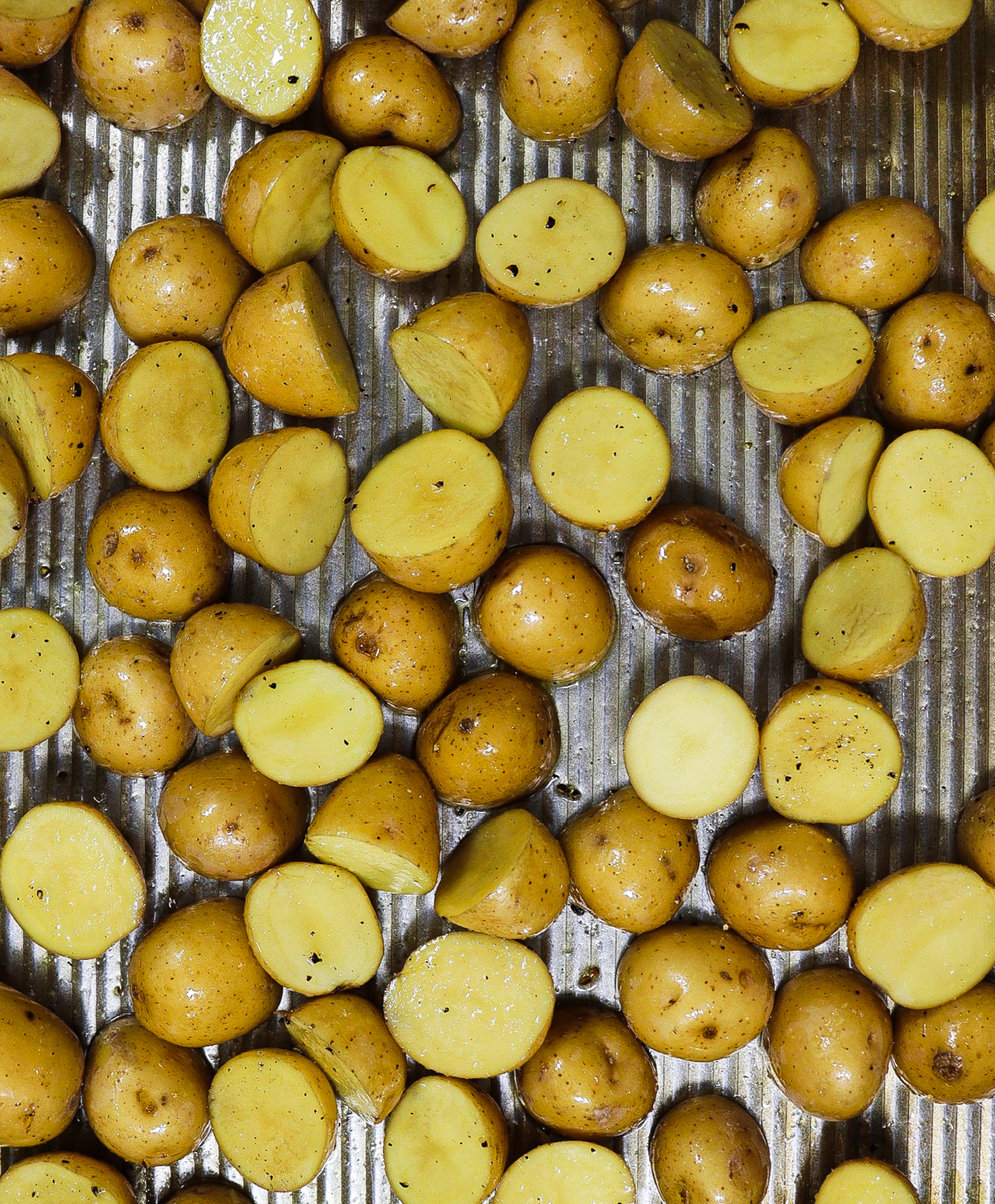Baking sheet with baby potatoes cut in half tossed in olive oil, salt and pepper, ready to be baked