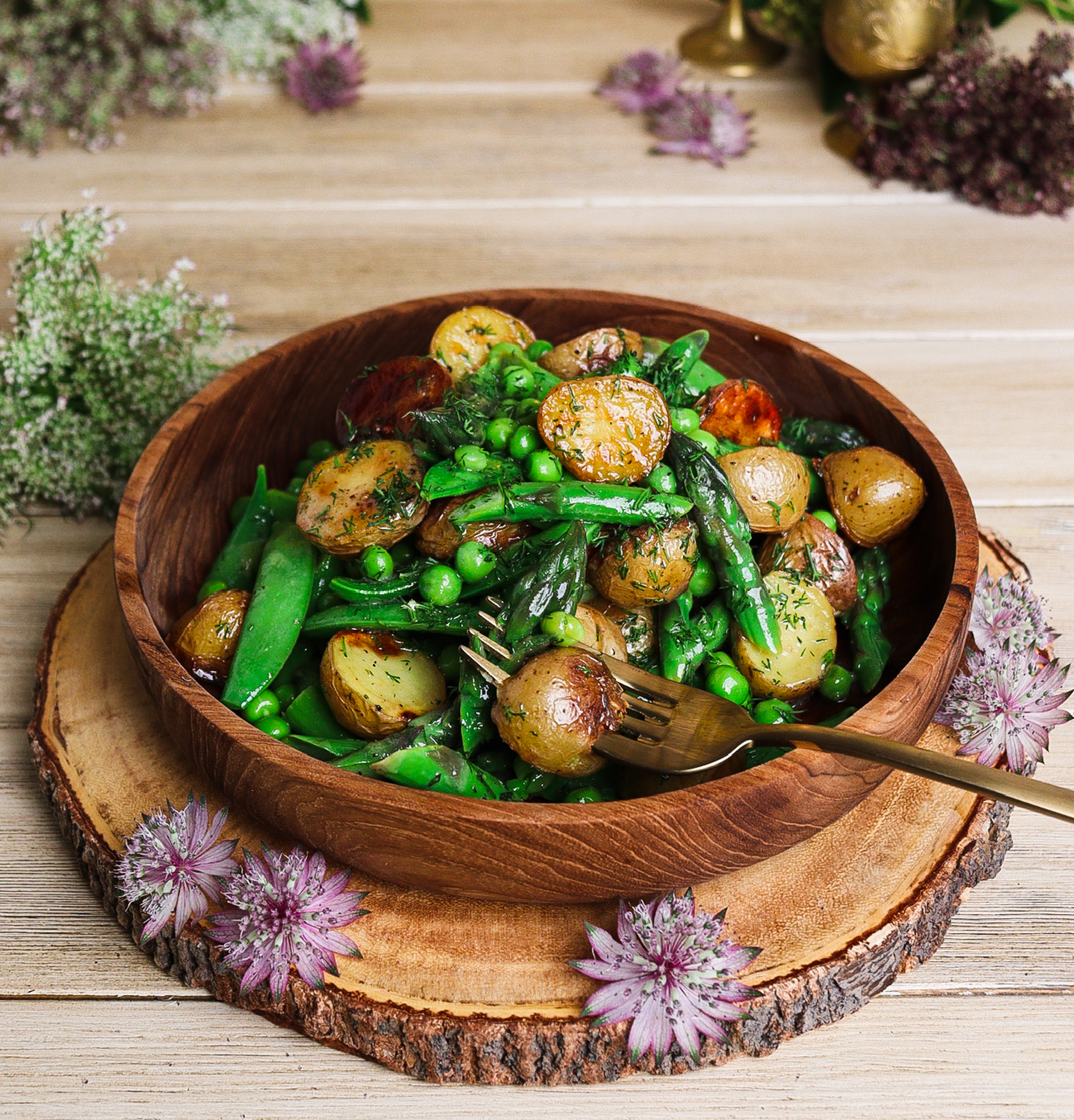 warm potato asparagus and pea salad in a rustic bowl surrounded by florals to evoke Lothlórien of Middle Earth